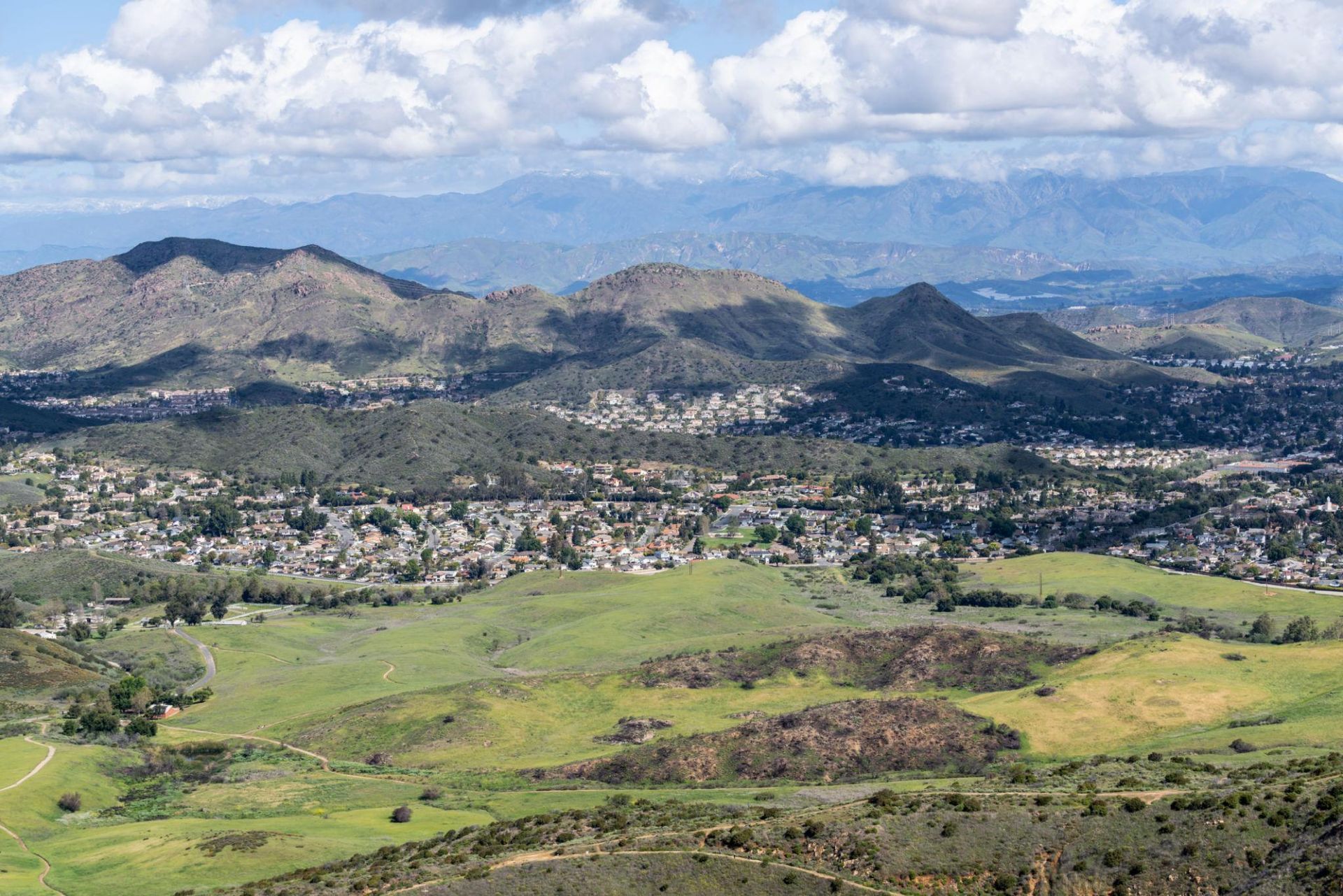 Panoramic view of a green valley, suburban town, and rocky mountains under a cloudy sky