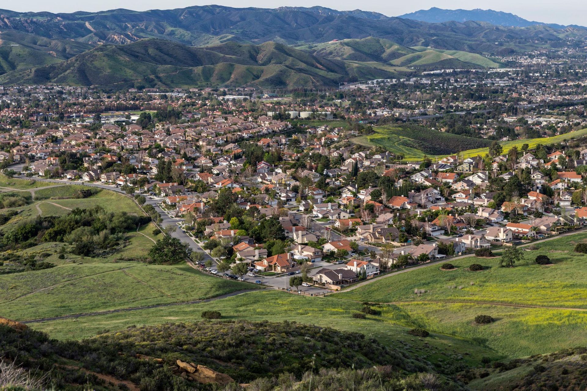 Wide view of a town in a green valley with hills and mountains in the background