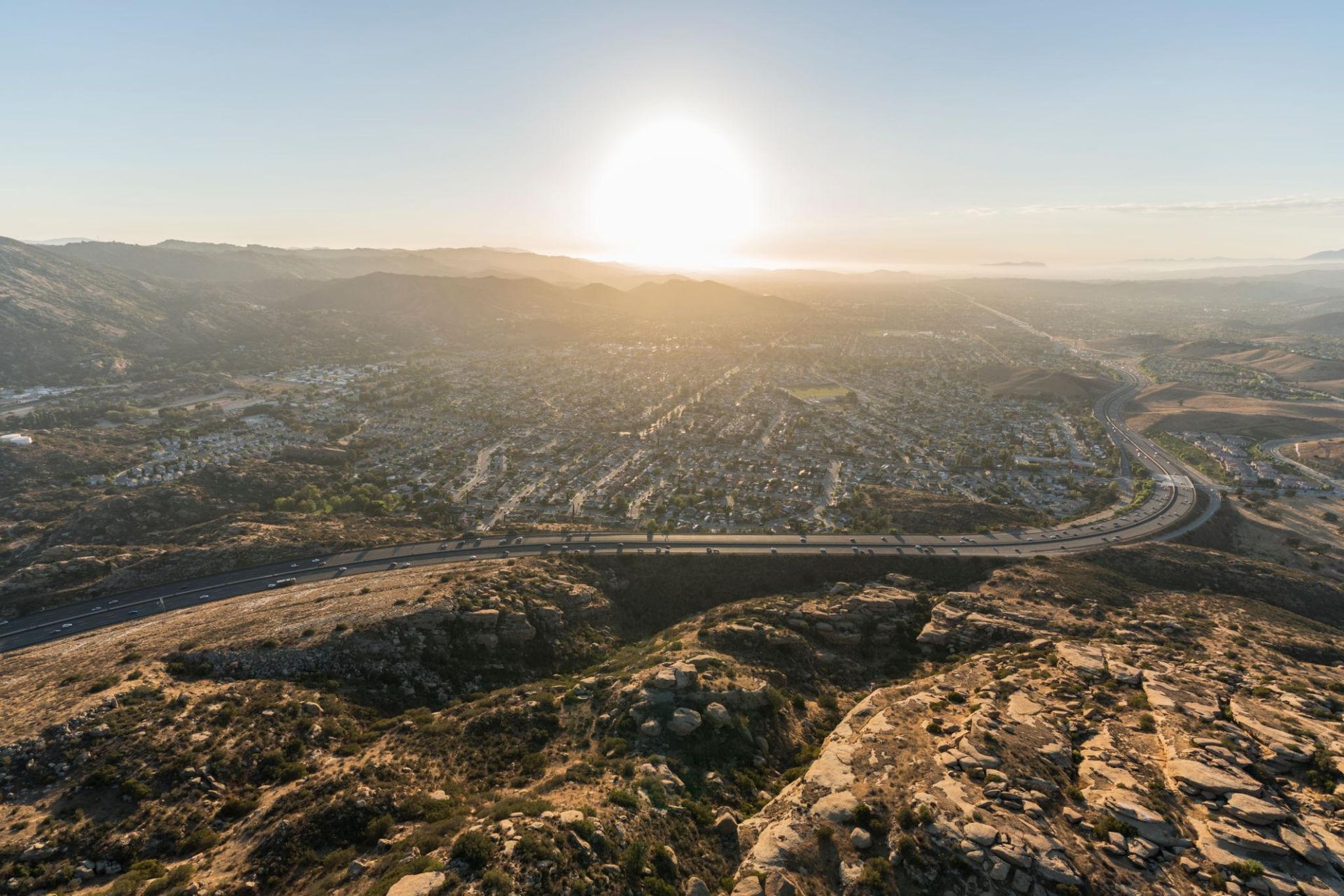 Sunrise over a sprawling city valley with highways and rocky hills in the foreground