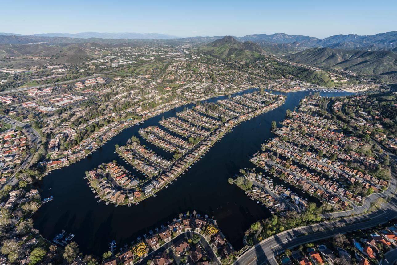 Aerial view of a coastal canal lined with dense waterfront homes and hills in the distance