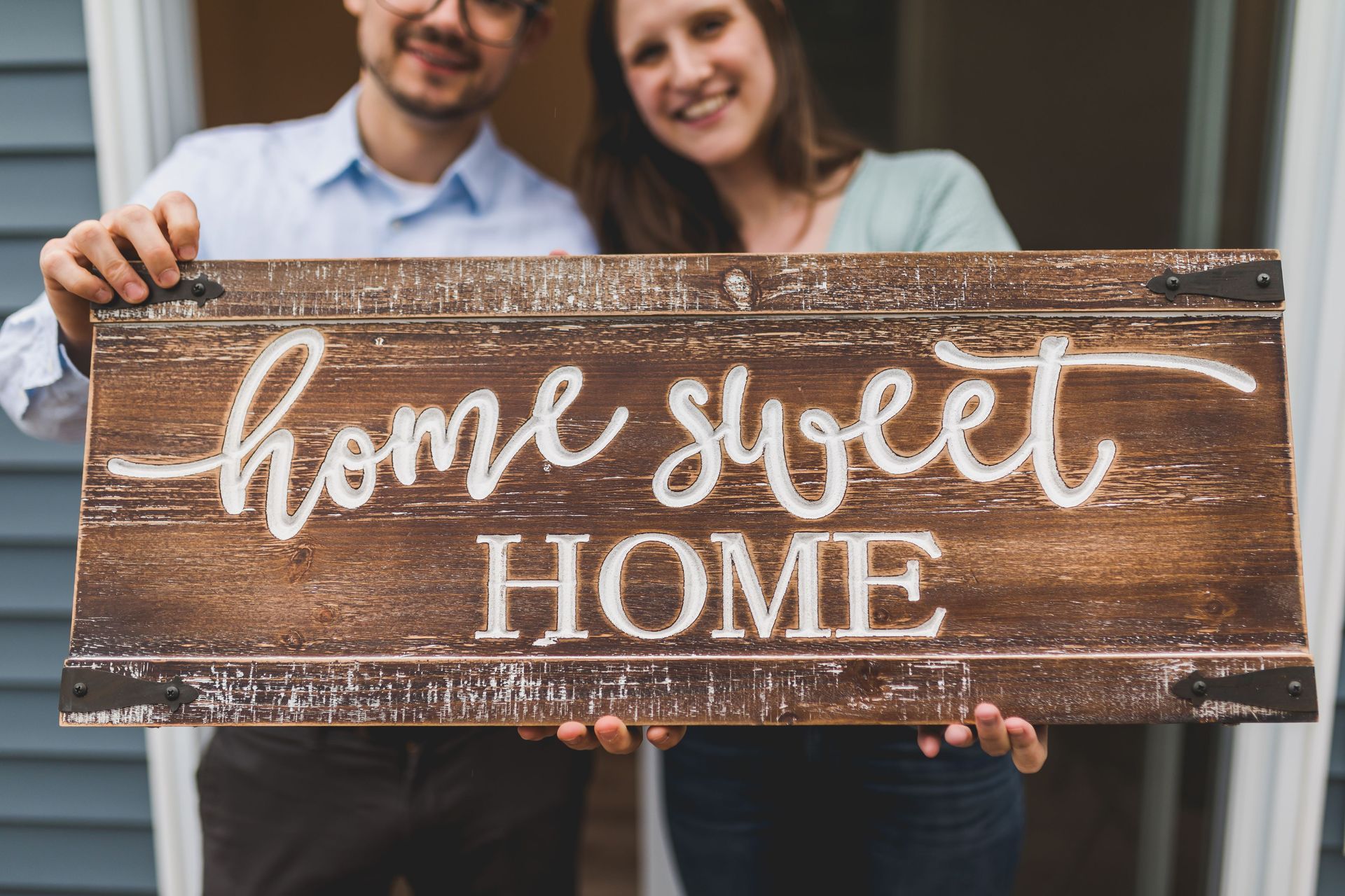 Couple holding a wooden “home sweet home” sign on a porch