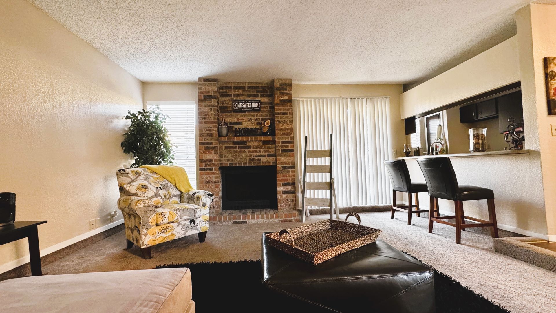 Cozy living room with brick fireplace, patterned armchair, bar with stools, and sliding glass doors.