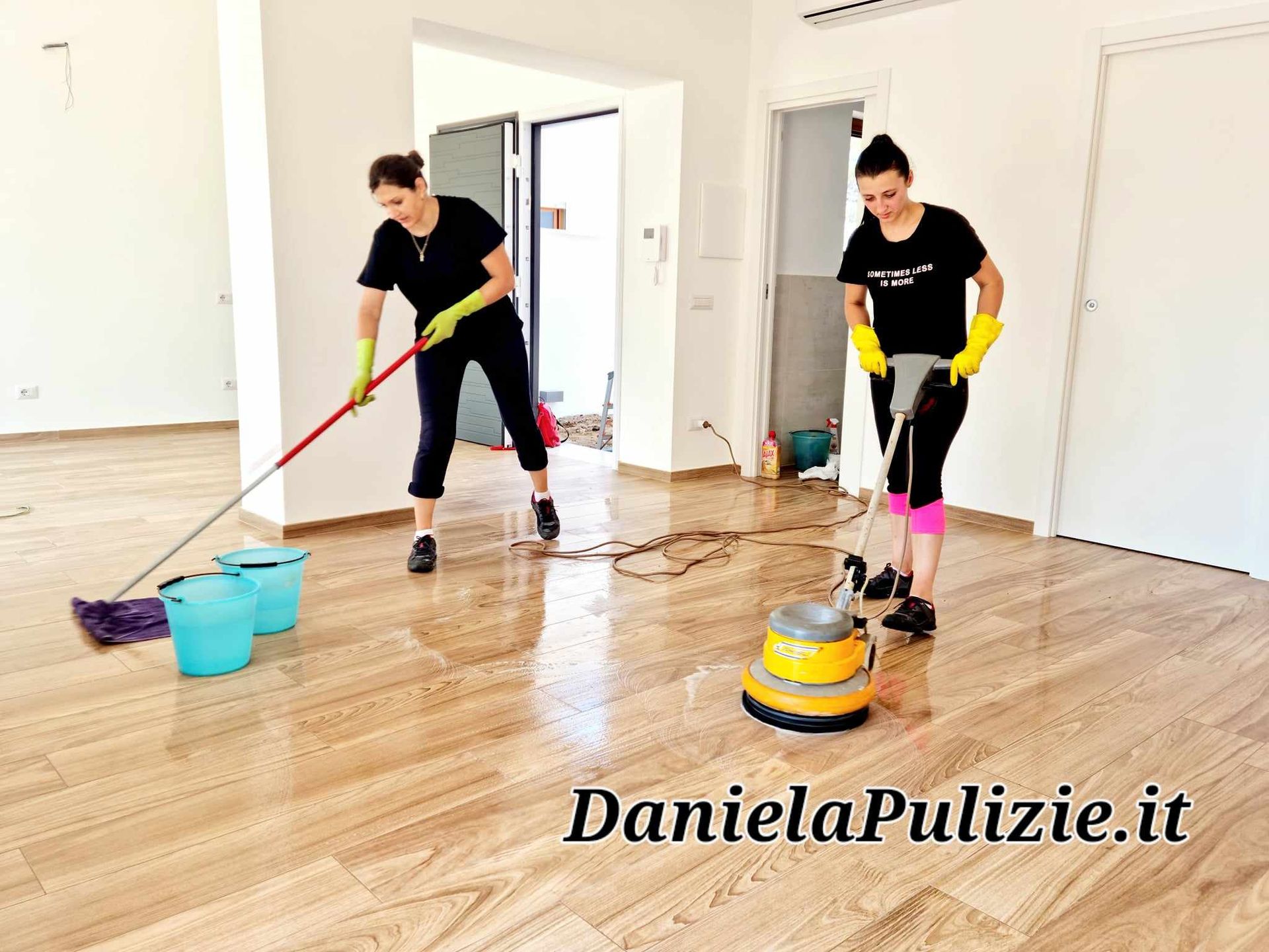 Due donne puliscono un pavimento in legno con mocio e lucidatrice in una stanza vuota.