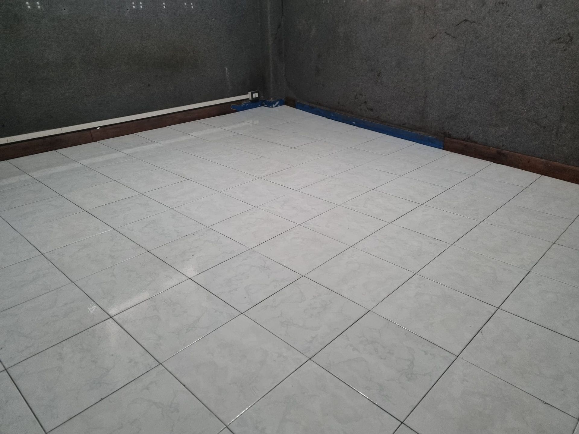 Stanza vuota con pavimento piastrellato bianco, pareti grigie e finiture marroni.