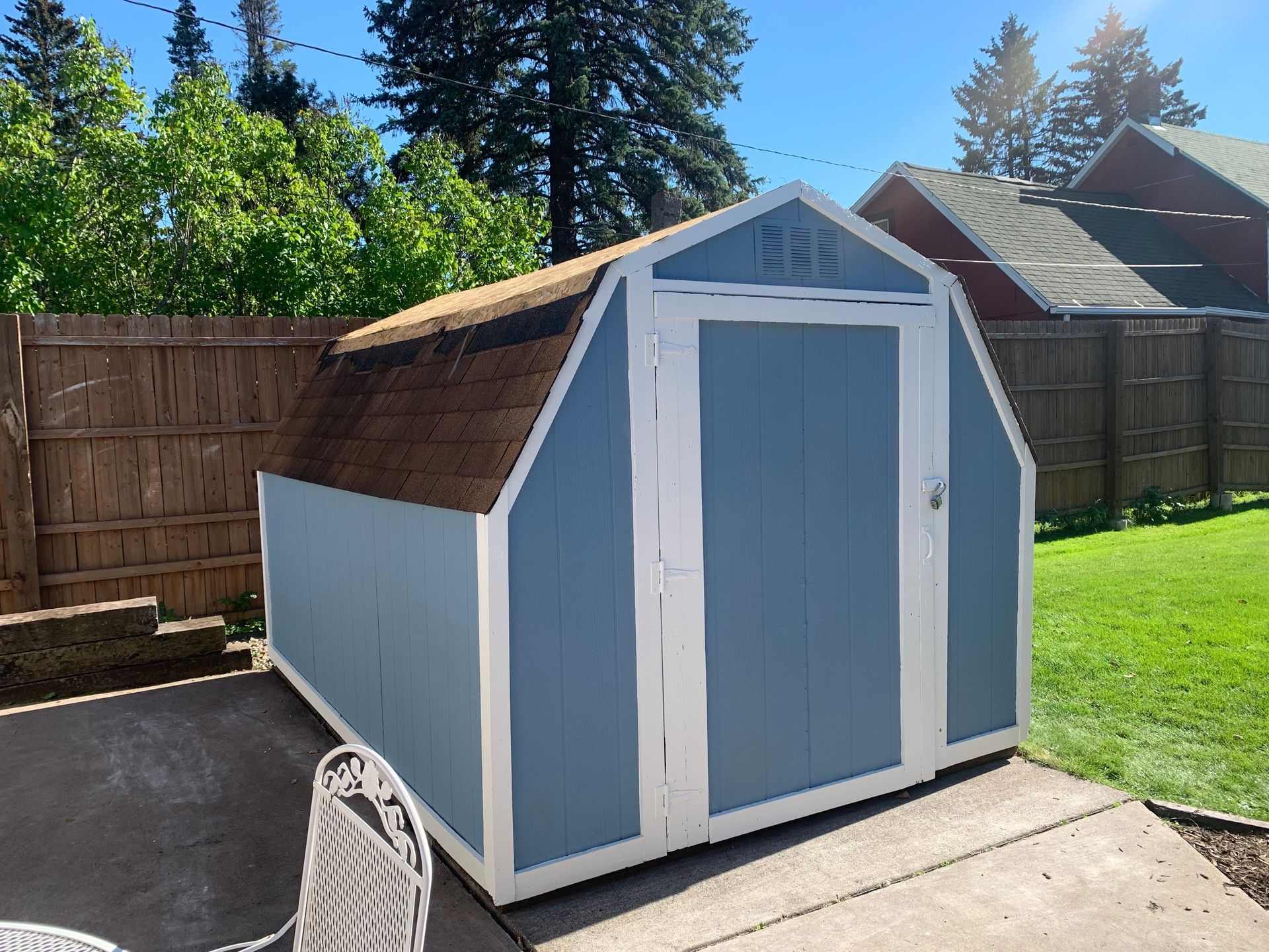 Blue-and-white backyard storage shed with barn-style roof and double doors in a sunny fenced yard
