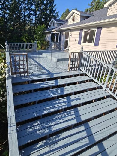 Front steps and a light blue deck with white railings beside a beige house in sunlight