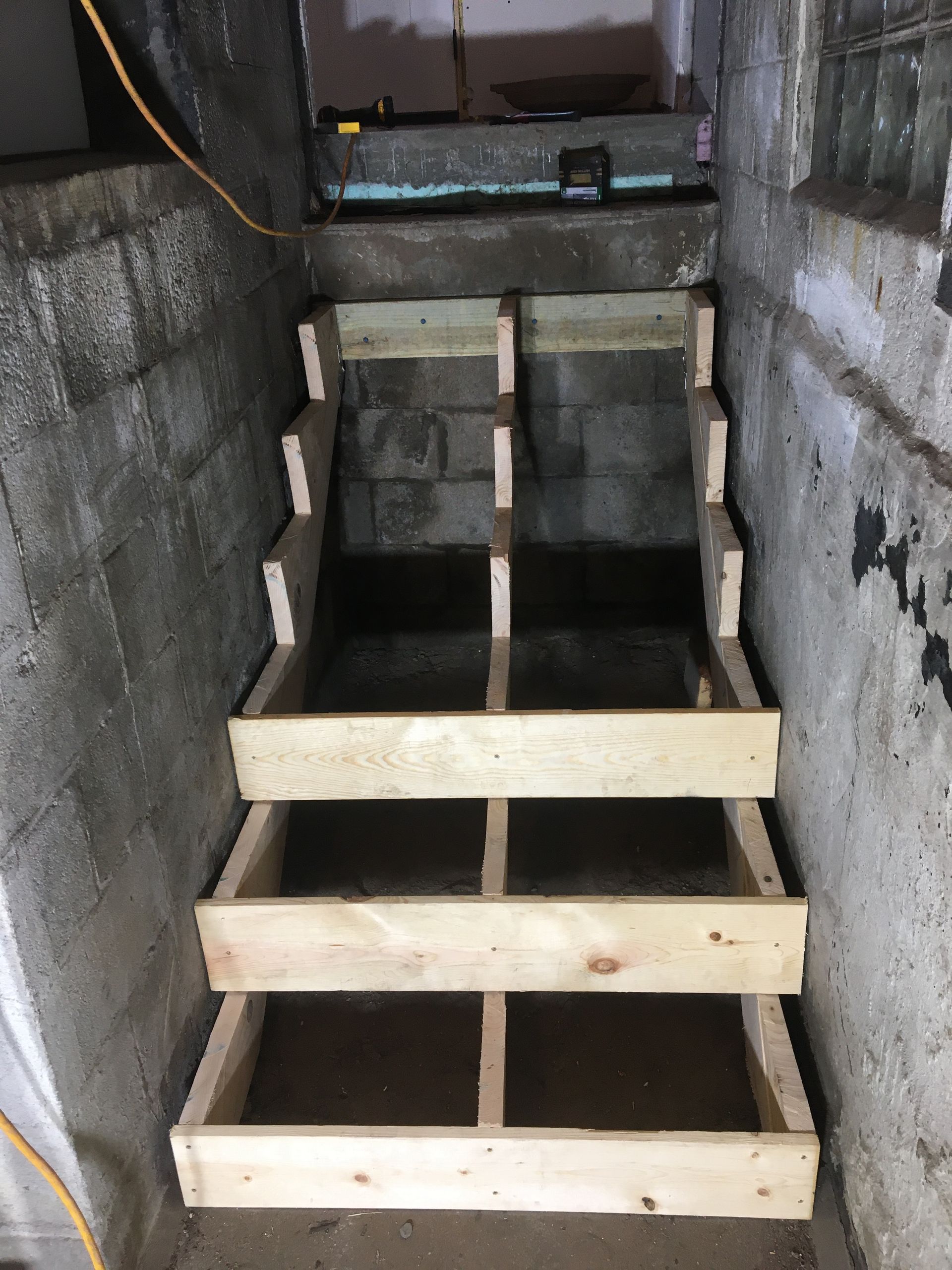 Partially built wooden stairs in a narrow concrete stairwell, leading down into darkness