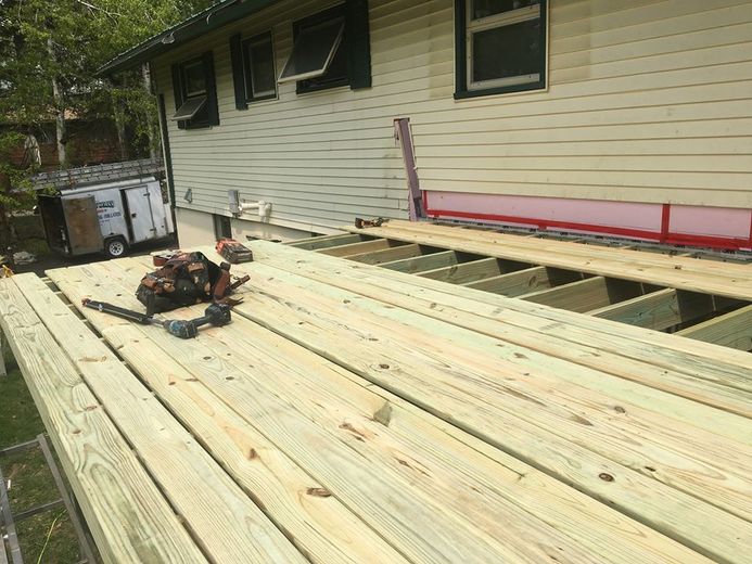 Partially built wooden deck beside a house, with tools and lumber laid across the joists.