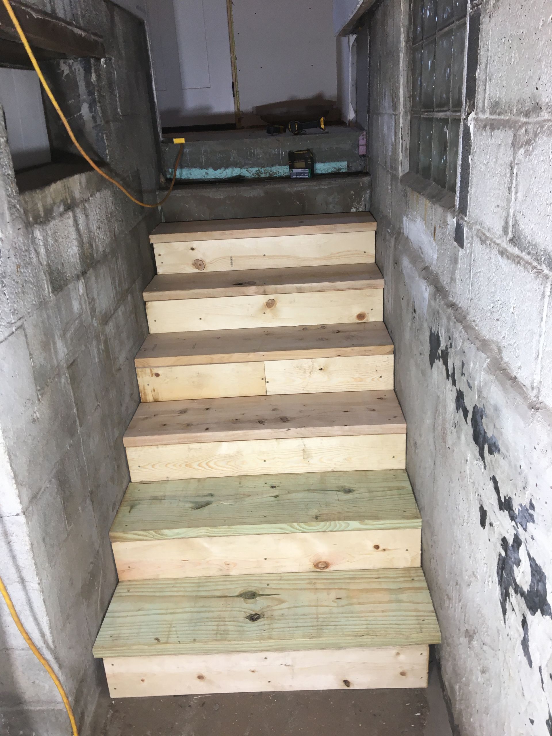 Unfinished wooden stairs in a narrow concrete stairwell under construction