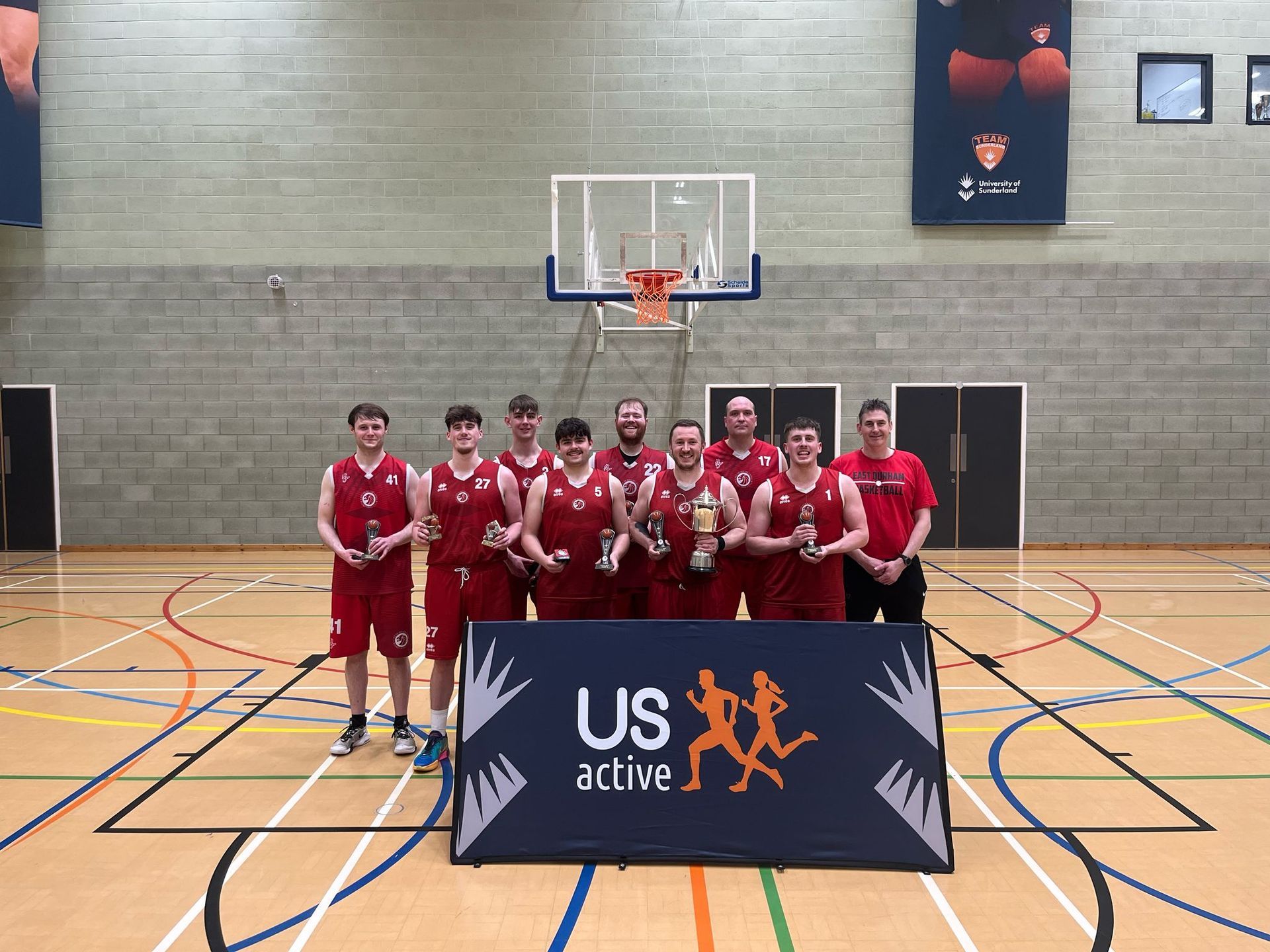 Basketball team in red uniforms posing indoors behind a US Active banner