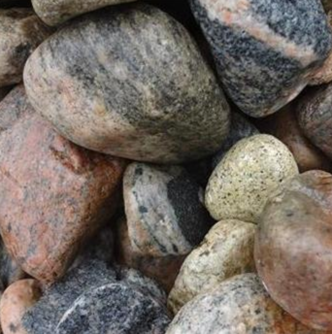A close-up view of various smooth, rounded river stones in shades of gray, brown, beige, and pink.