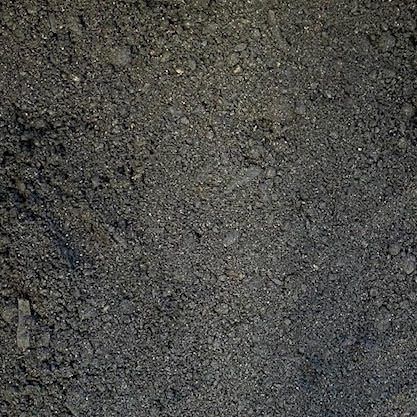 A close-up, top-down view of dark gray, fine-grained soil or crushed gravel with a coarse, uneven texture.