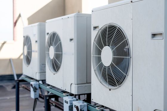 Three white air conditioning units on a rooftop, lined up, with large fans visible.