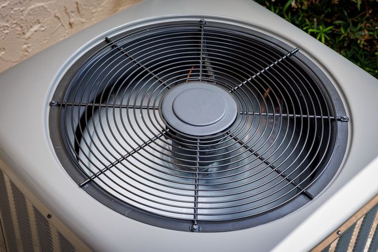 Close-up of an air conditioning unit's fan, with a gray metal grill, and a light-colored casing.
