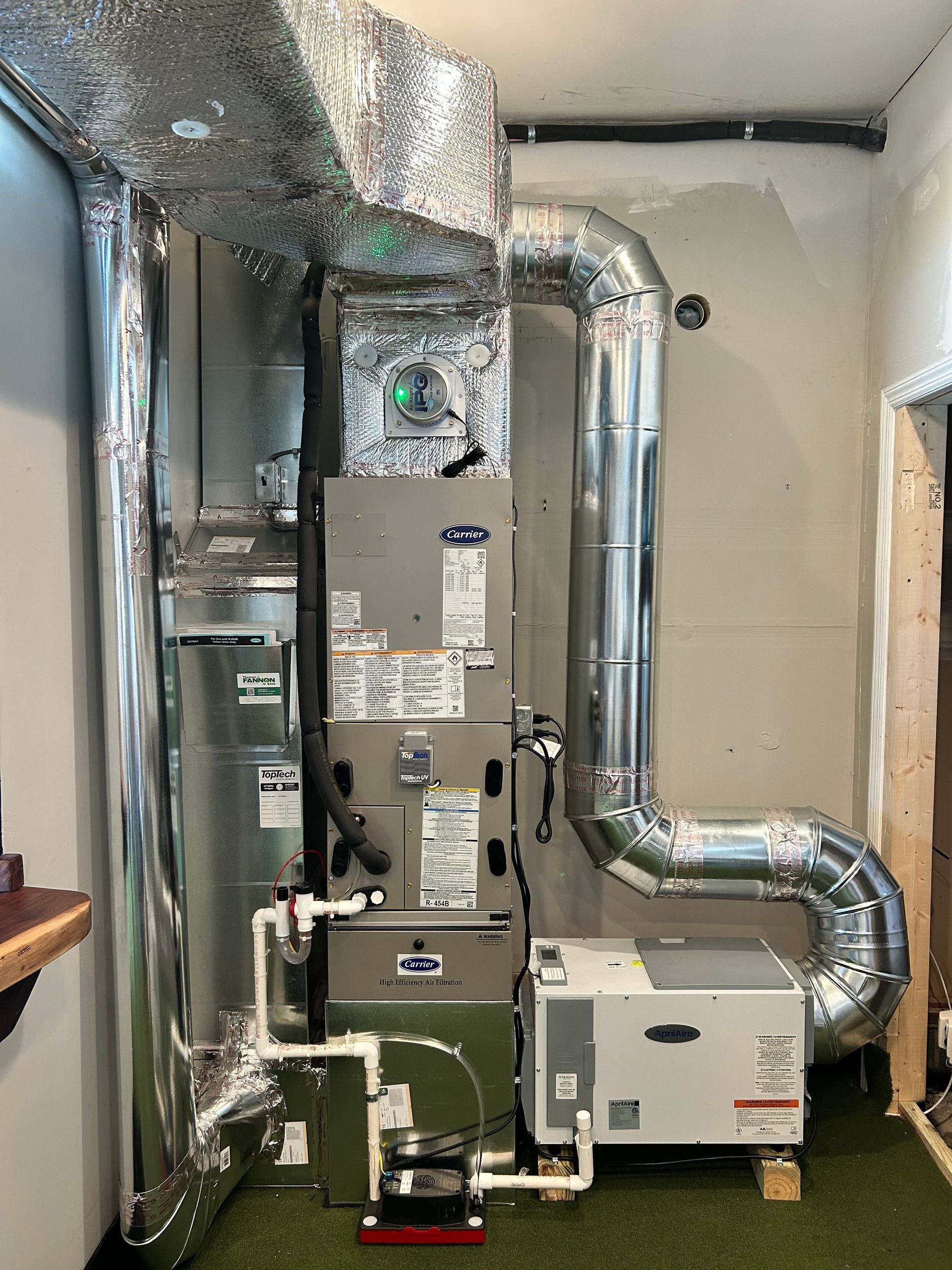 A furnace and humidifier installed in a room. Silver ductwork and equipment against a white wall.