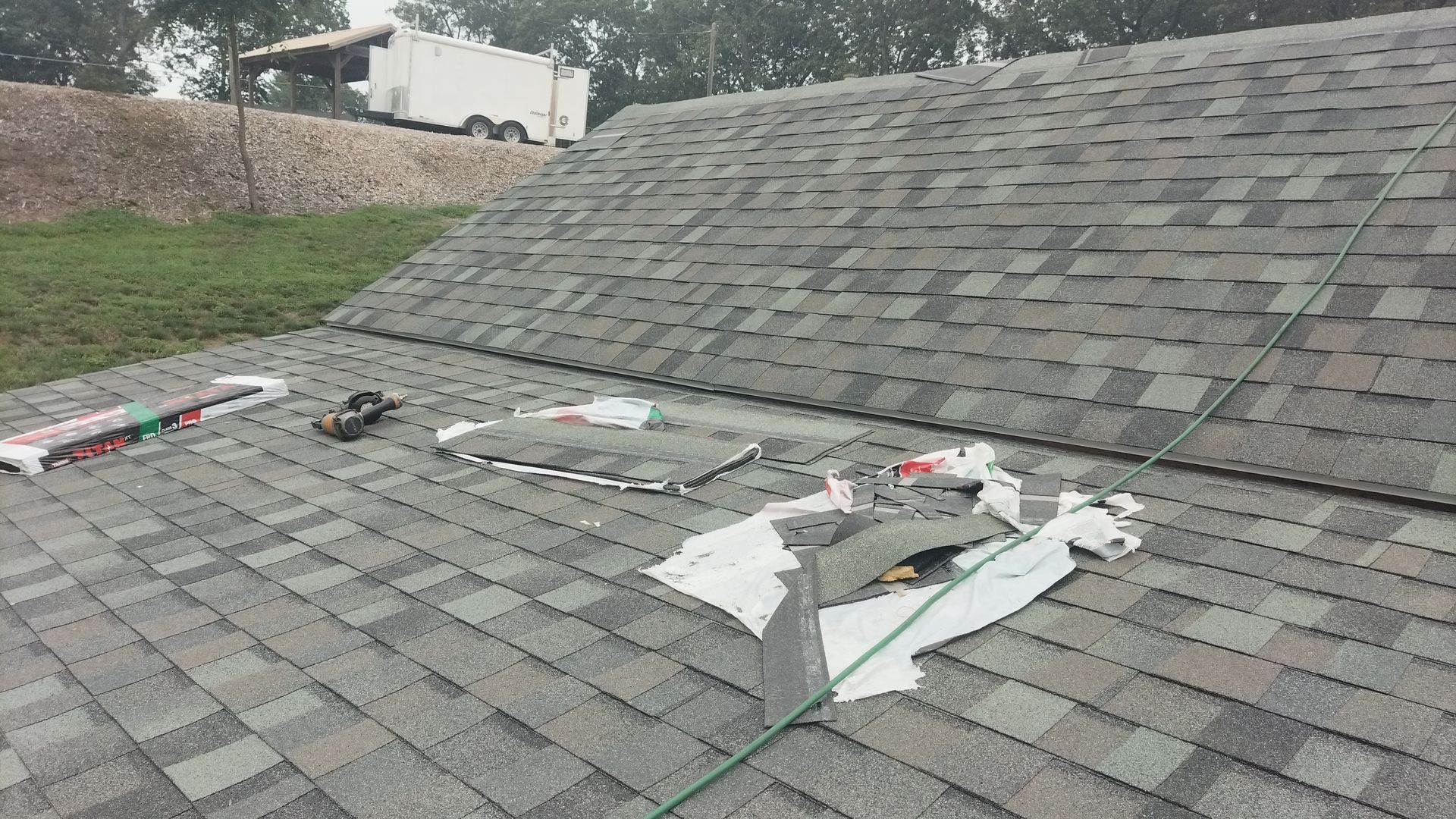 Roofer using a nail gun to install asphalt shingles on a roof.