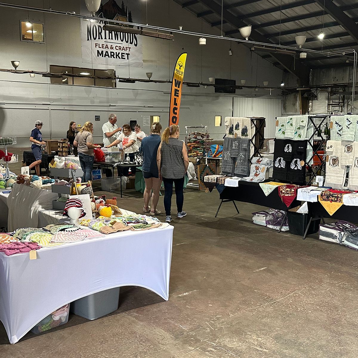 Indoor market with vendor tables and shoppers under hanging signs and lights