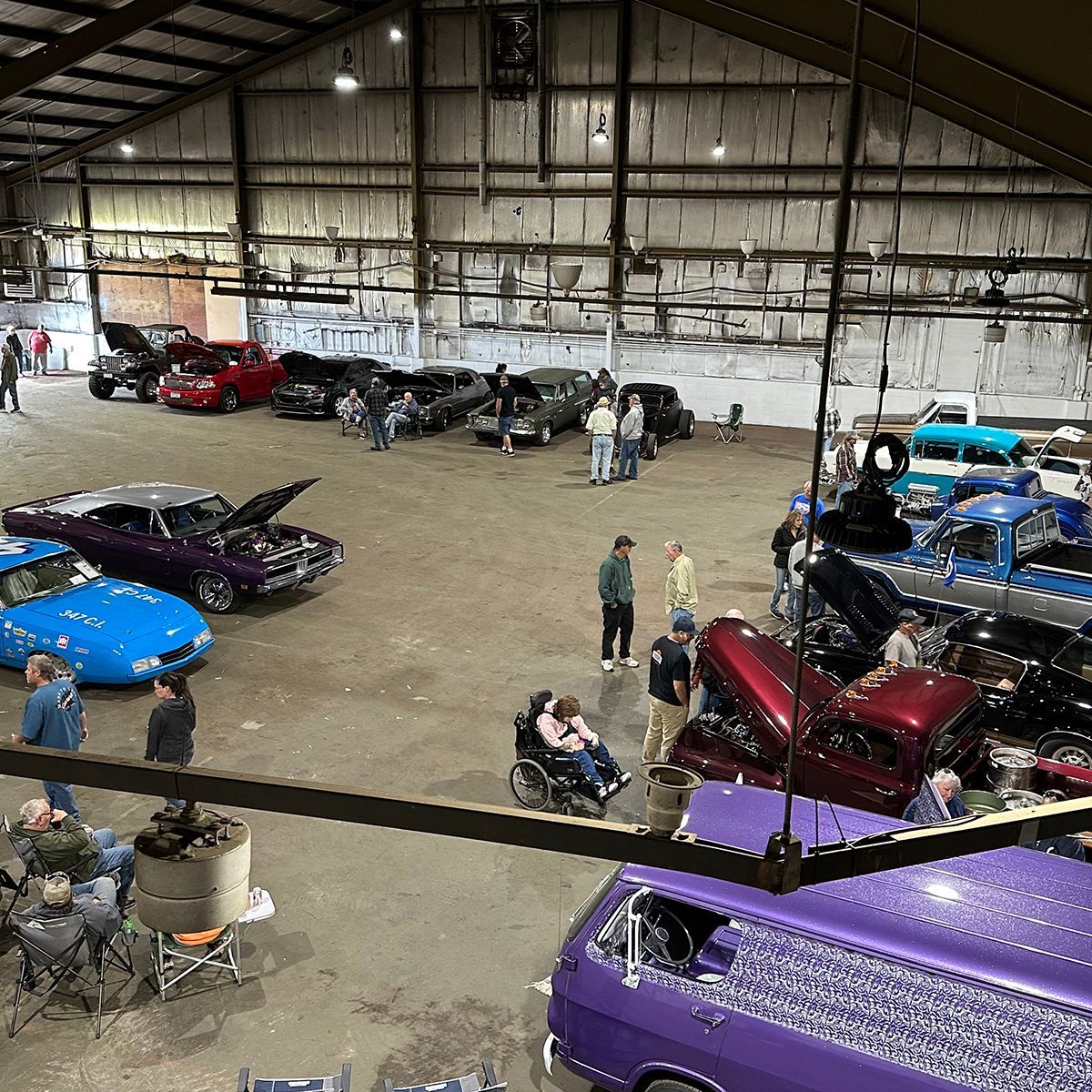 Classic cars displayed in a large warehouse, with people walking among rows of colorful vehicles