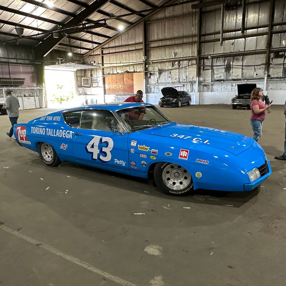 Blue race car number 43 in a warehouse with people standing nearby at a  classic car show, Hill City, MN