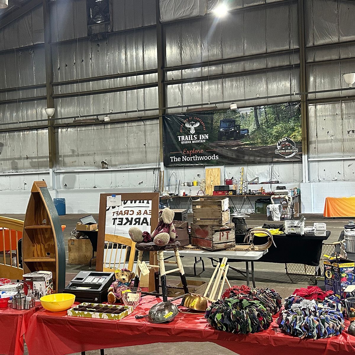 Indoor flea market tables filled with handmade goods, toys, and crafts under a high warehouse ceiling