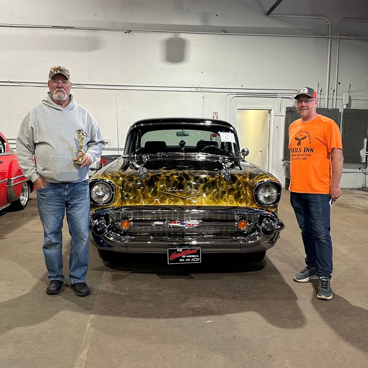 Two people standing beside an award-winning classic black car with gold floral decorations at a classic car show