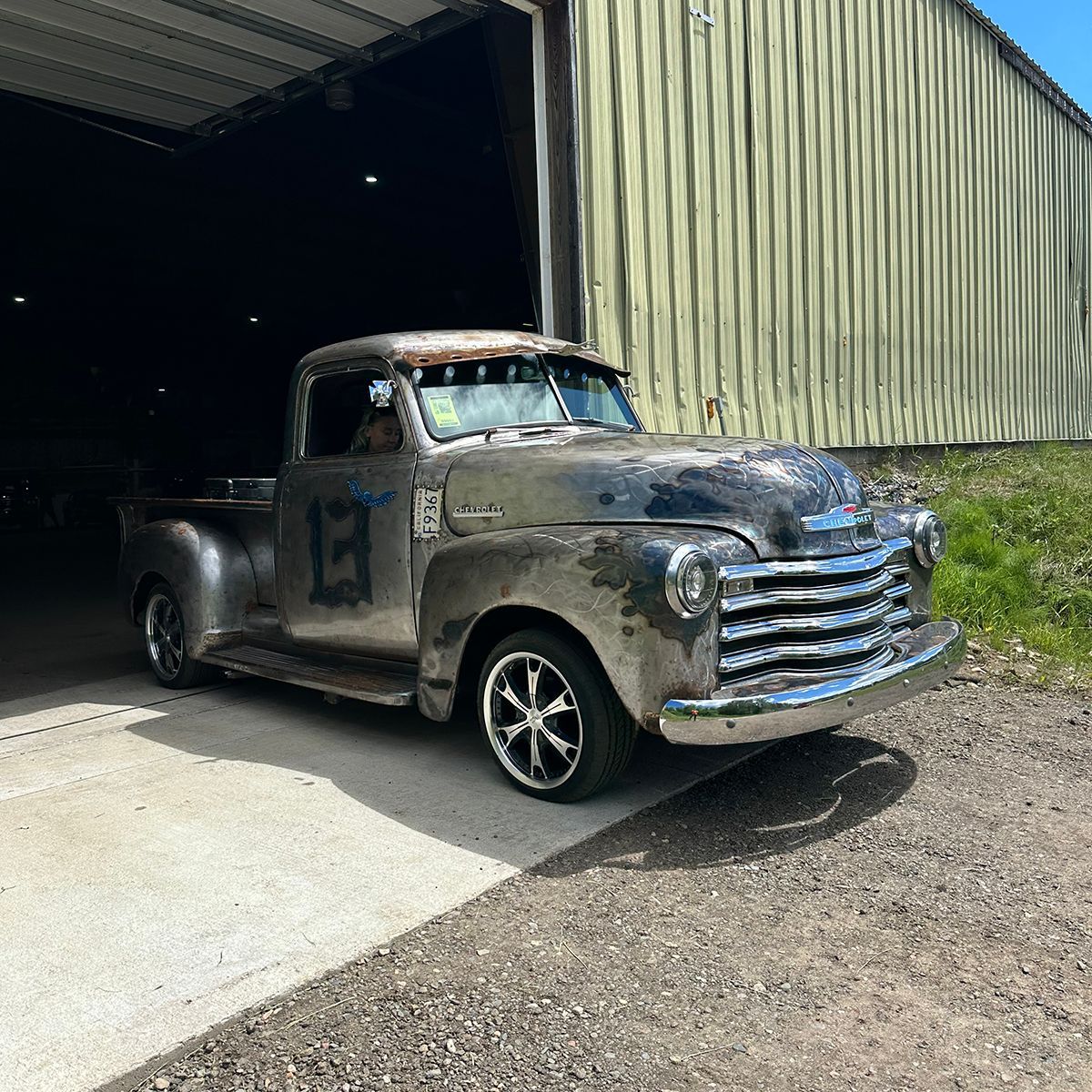 Rusty vintage pickup truck parked partly in a barn doorway and warehouse on a gravel driveway