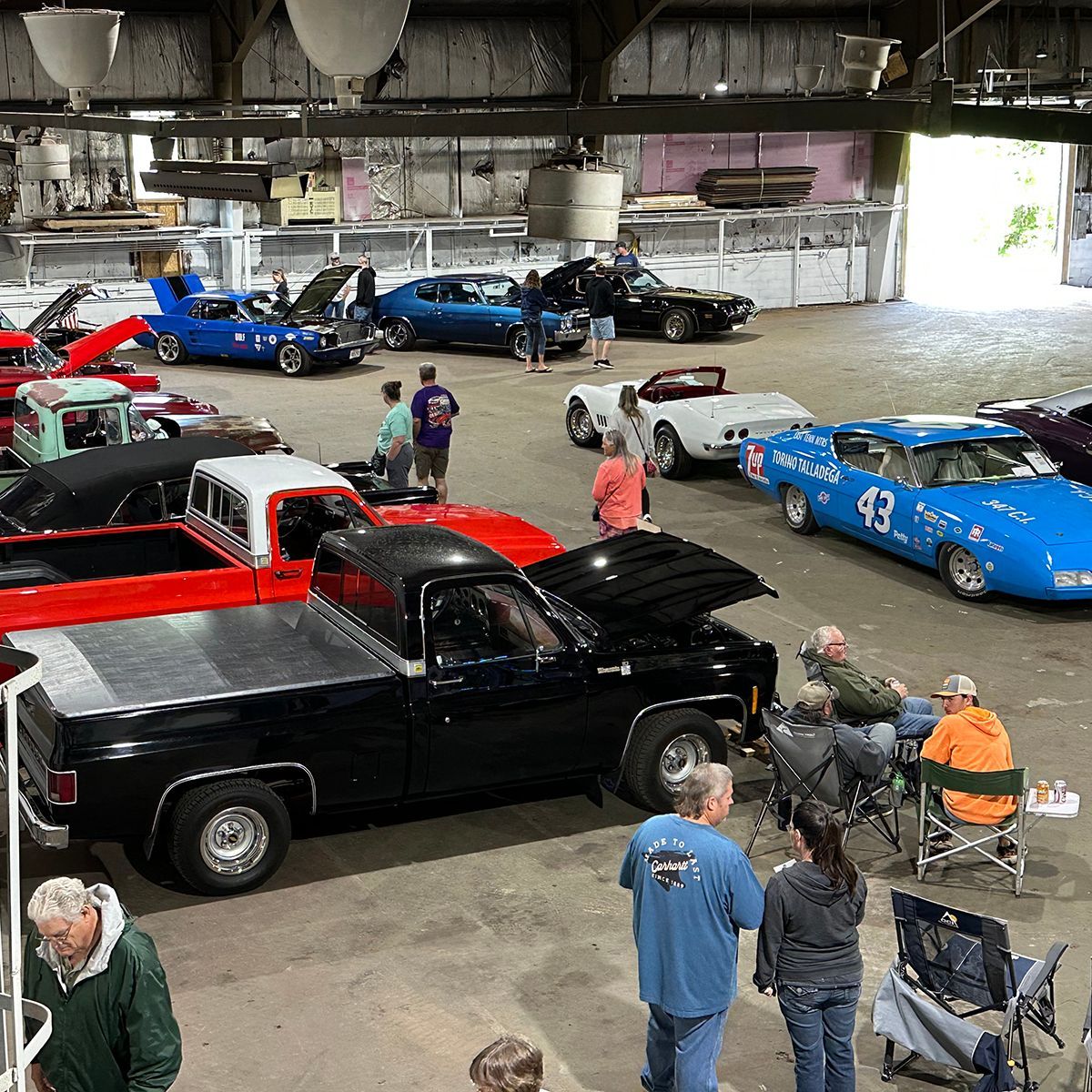 Classic car show inside a warehouse, with several vintage cars and people gathered around them