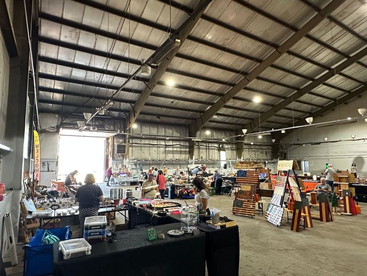Inside image of Northwoods Flea & Craft Market with tables, clothing racks, and shoppers under a high metal roof.