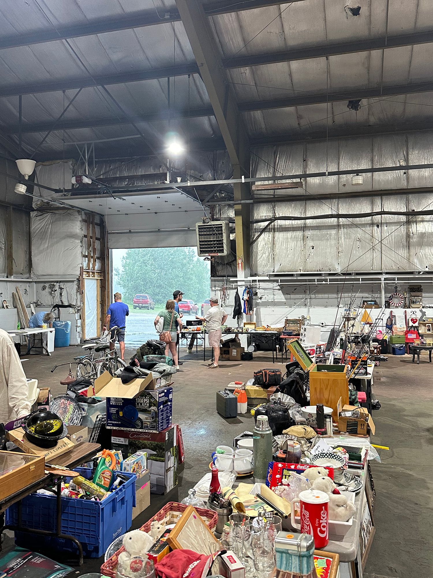 Warehouse-like hall filled with boxes and supplies, with people sorting items near an open loading door