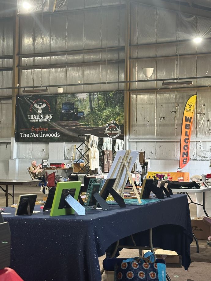 A vendor display table showing various framed images, products, and more at Northwoods Flea & Craft Market.