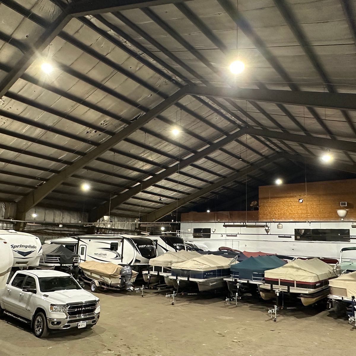 Indoor winter storage bay with several boats and vehicles parked under a lit metal roof at night