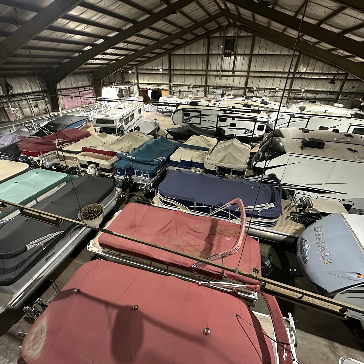 Indoor warehouse for winter storage, packed with rows of covered boats under a high metal roof
