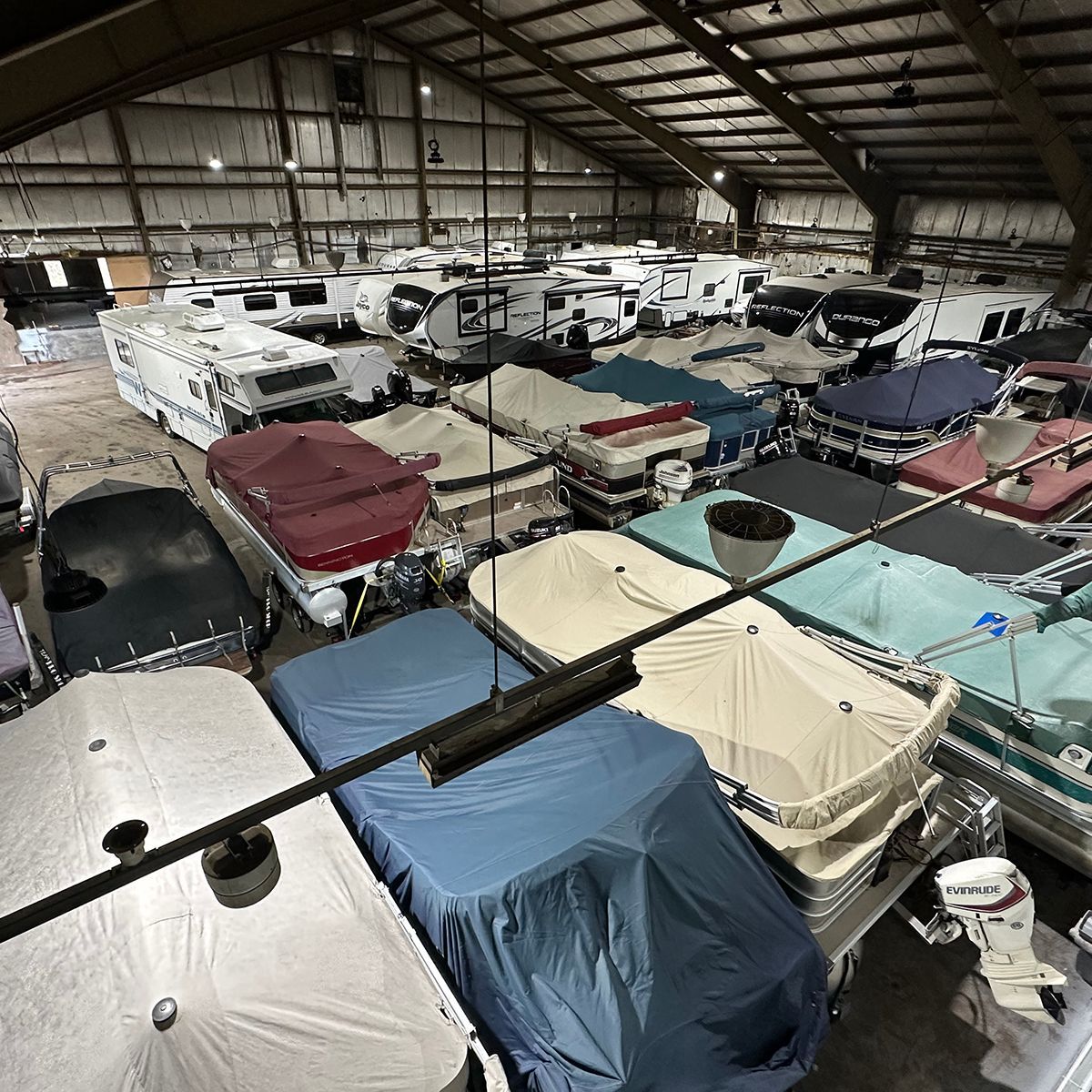 Large indoor metal warehouse for winter storage, full of covered boats and RVs packed in rows