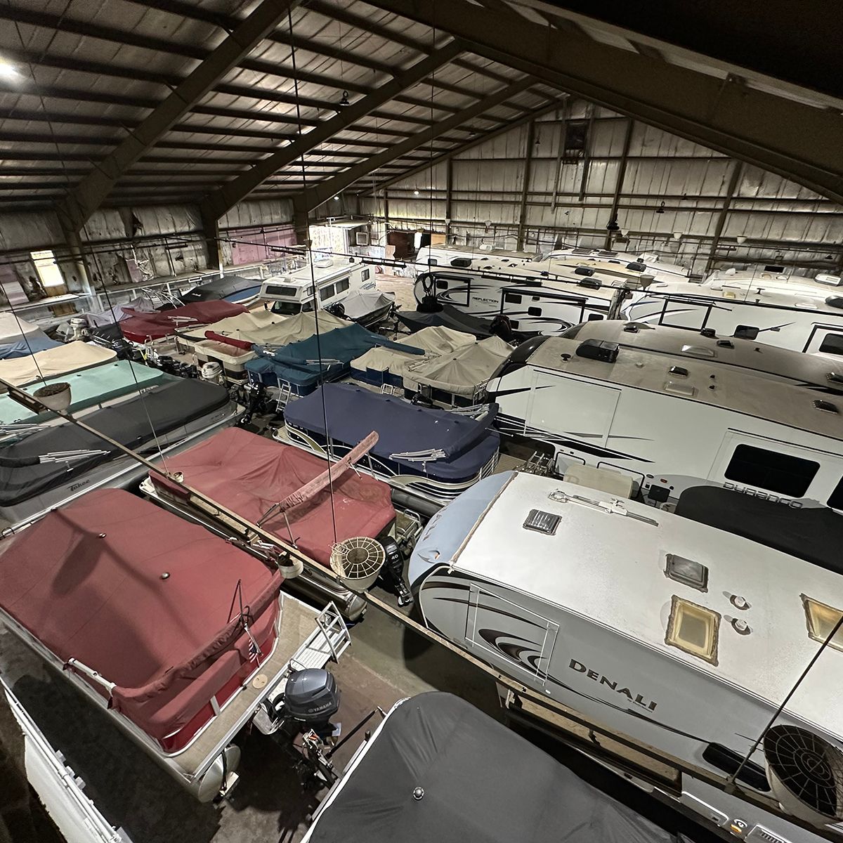 Indoor warehouse winter storage services for a packed row of covered boats and RVs under a high metal warehouse roof