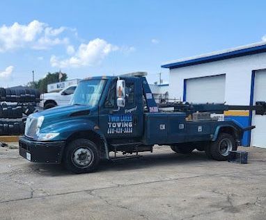 A blue tow truck is parked in front of a garage.