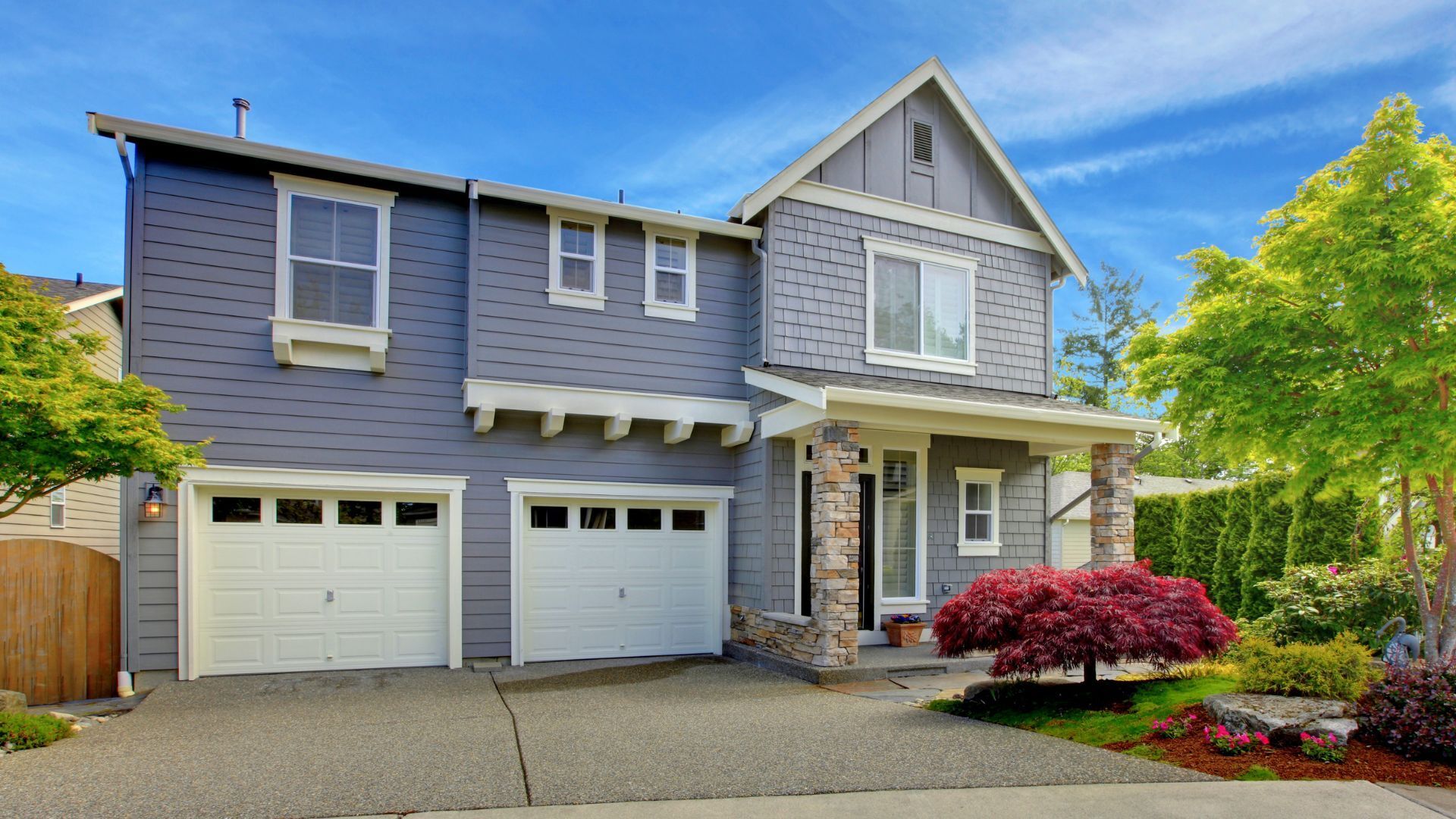 Two-story gray house with white trim, double garage, and landscaped front yard under a blue sky