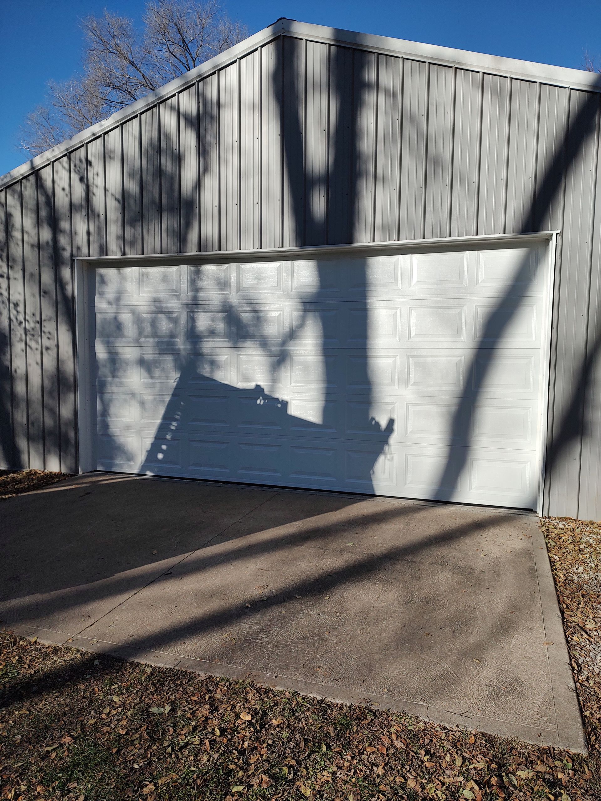 White garage with closed door, shadow of a tree across the facade, and a concrete driveway in front.