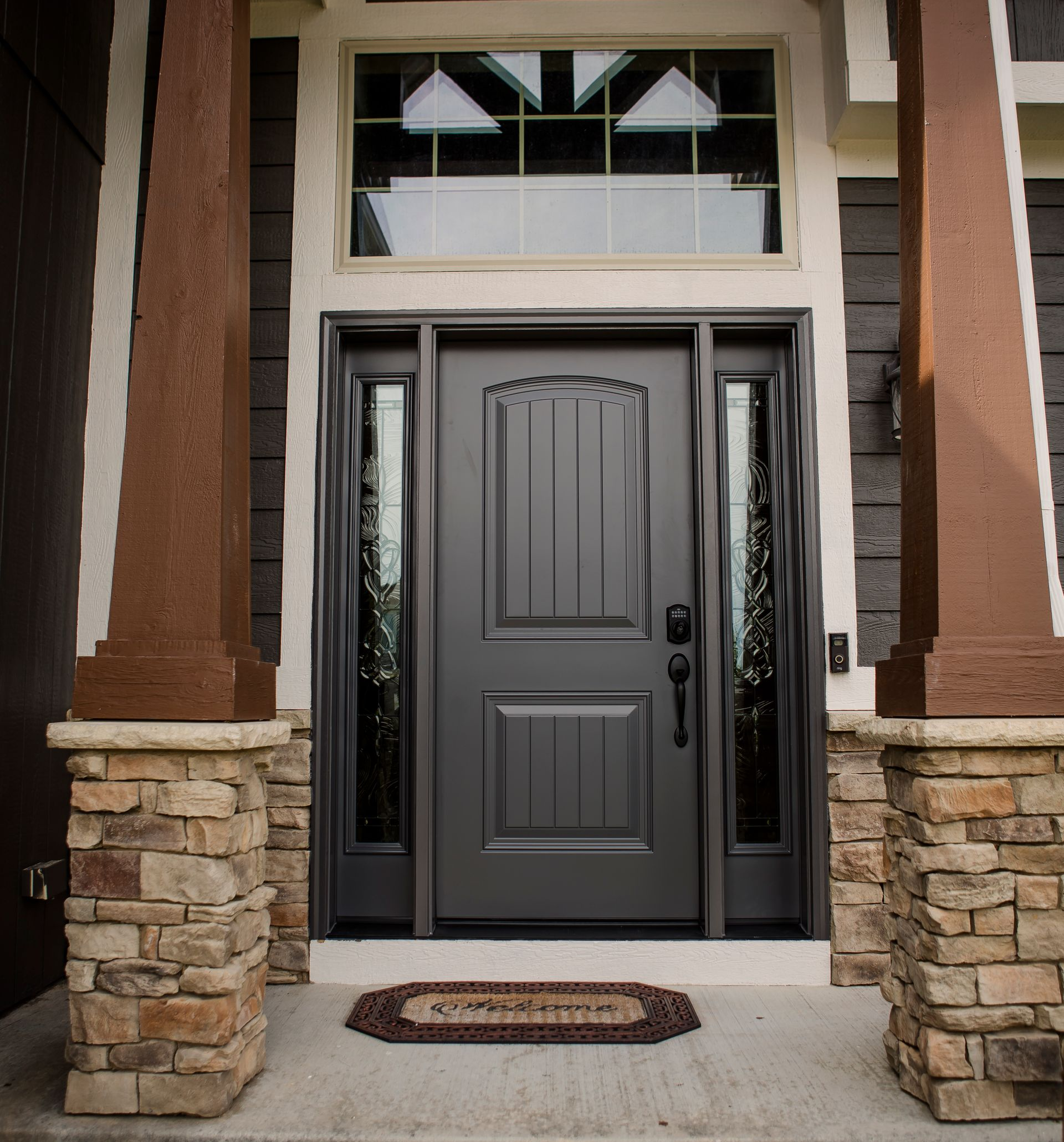 New dark brown front door with etched sidelights, a big window over the door, and stone pillars on a house porch