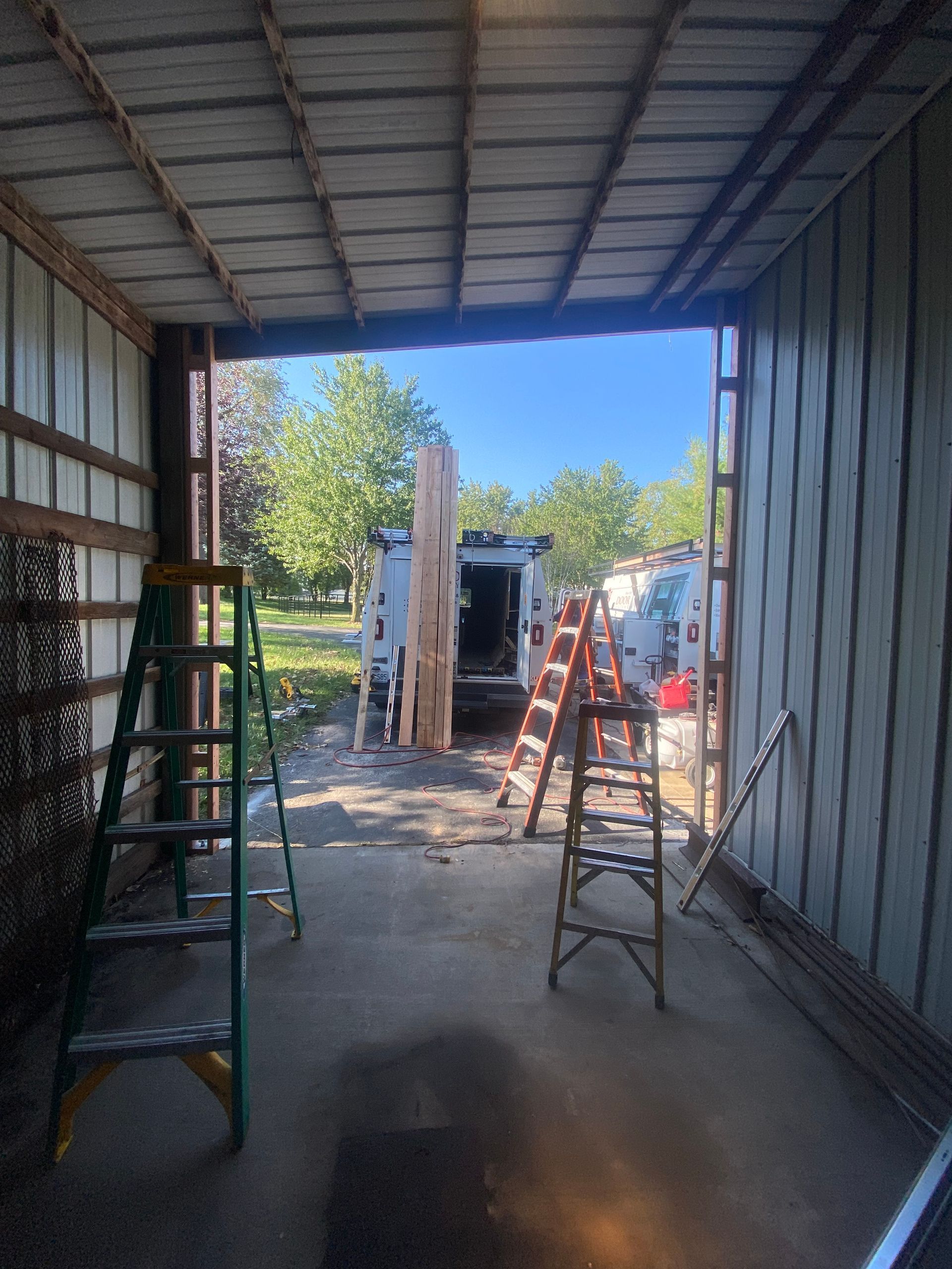 Container interior with ladders and construction materials, looking out to a sunny worksite.