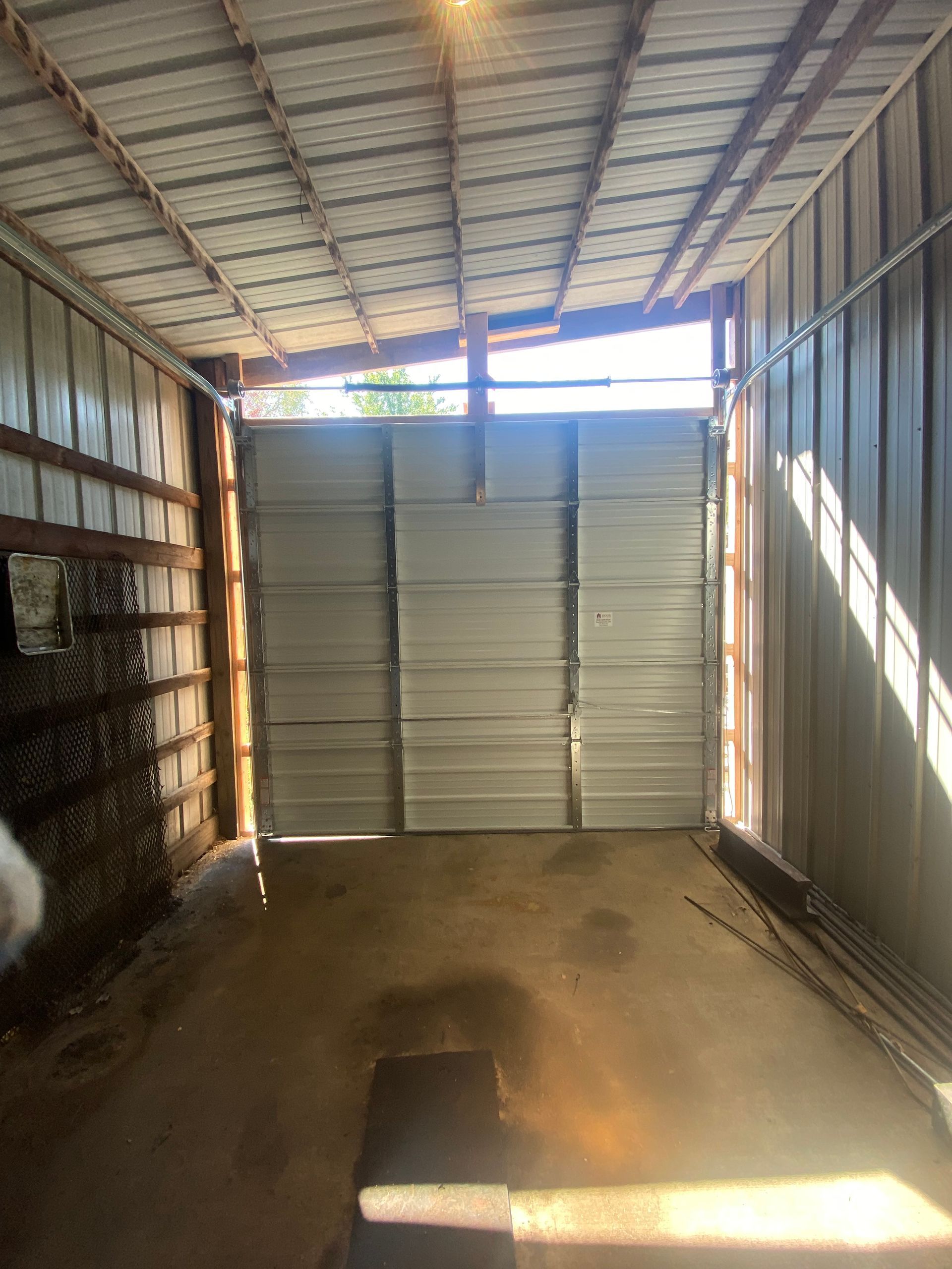Interior of an empty cargo truck with metal walls and closed rear doors, lit by sunlight.