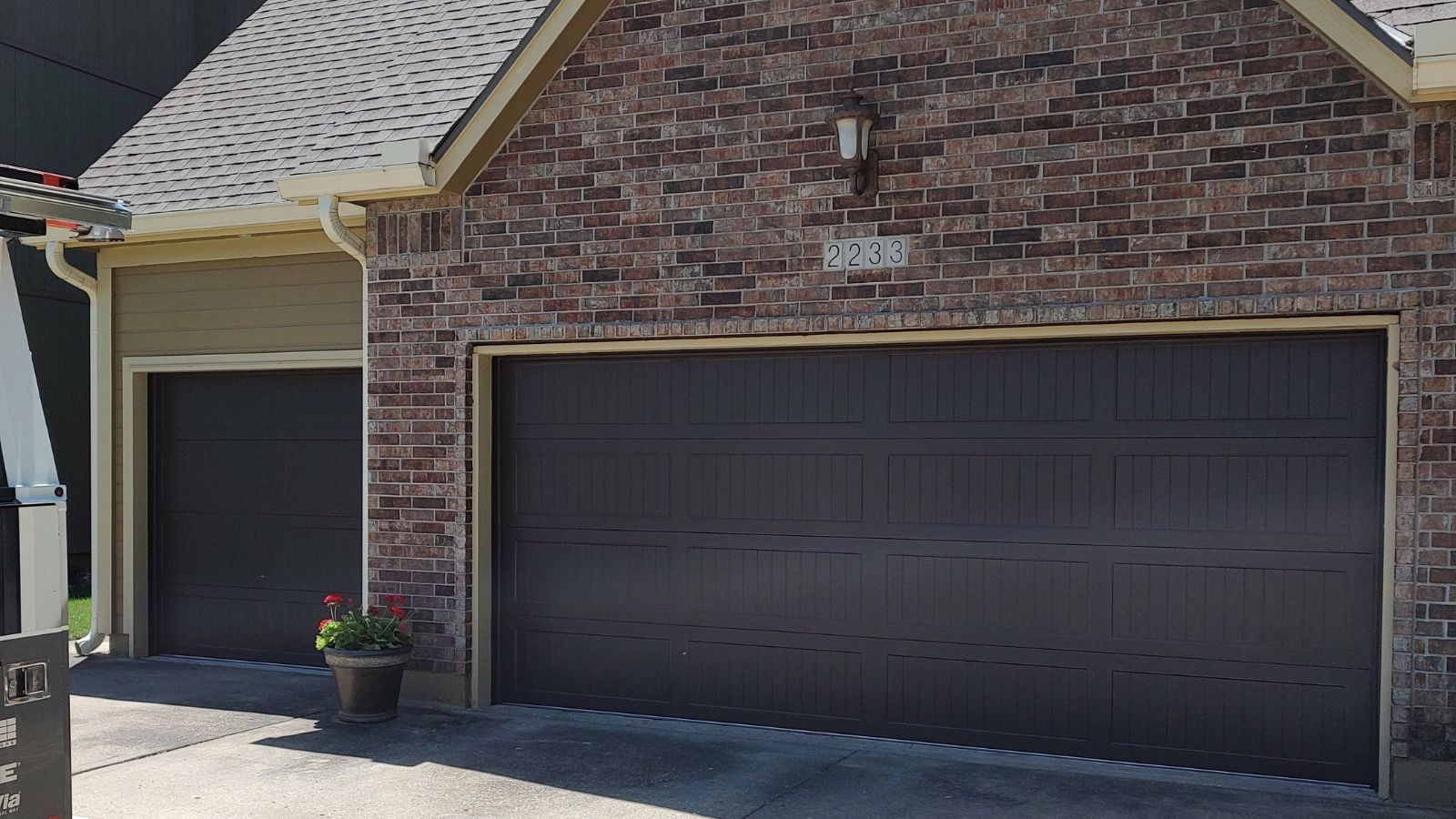 replace garage door A brick house with two garage doors and a potted plant