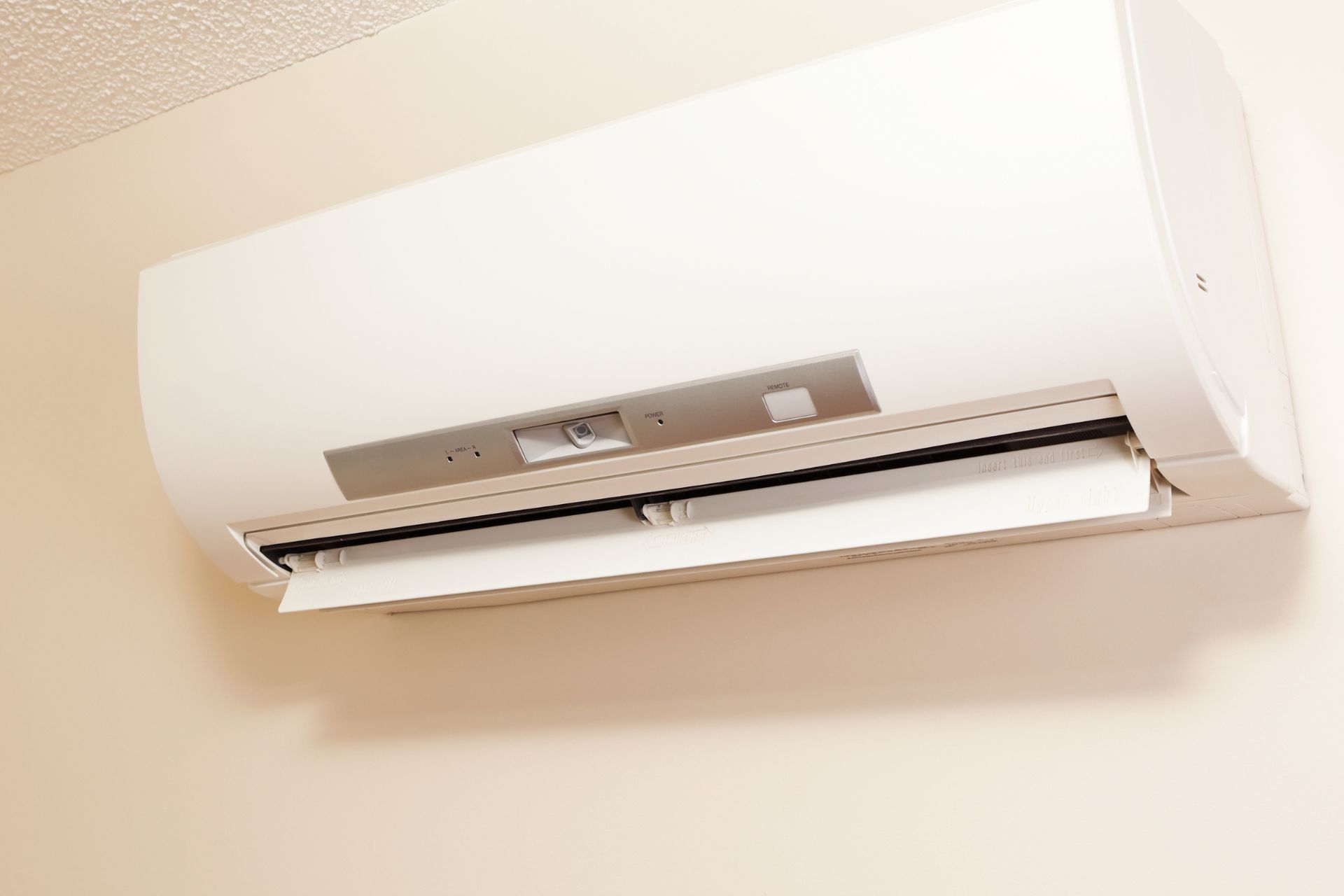 Wall-mounted white air conditioner on a beige wall with the vent open.