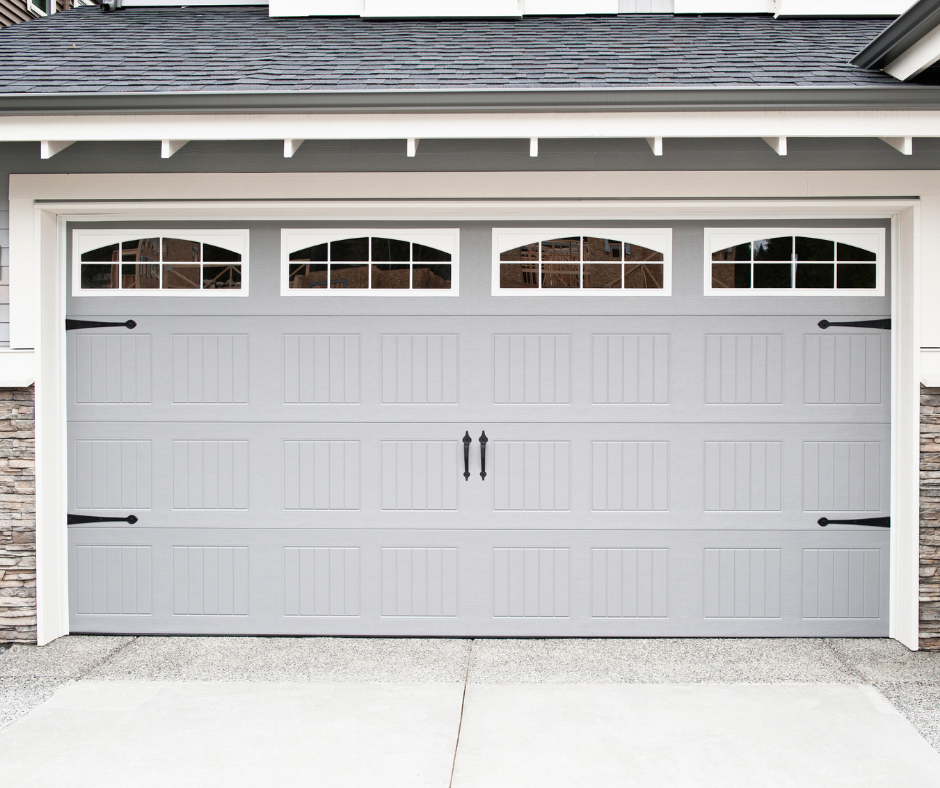 Light gray double garage door with four small arched windows and black handles under a white roofline