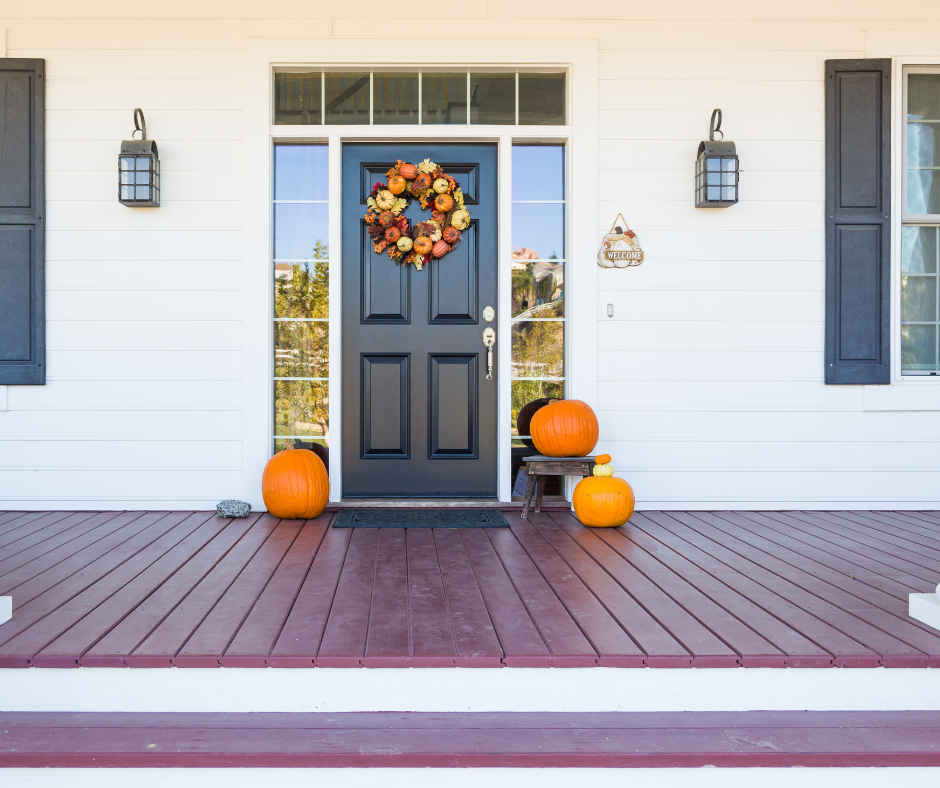 Front porch with a dark blue door, autumn wreath, pumpkins, and white siding with lantern lights.