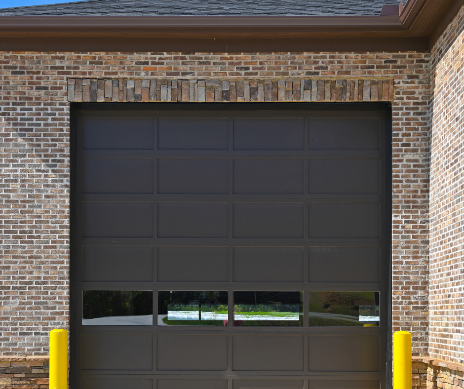 Closed dark gray garage door in a brick building, with yellow bollards on both sides.