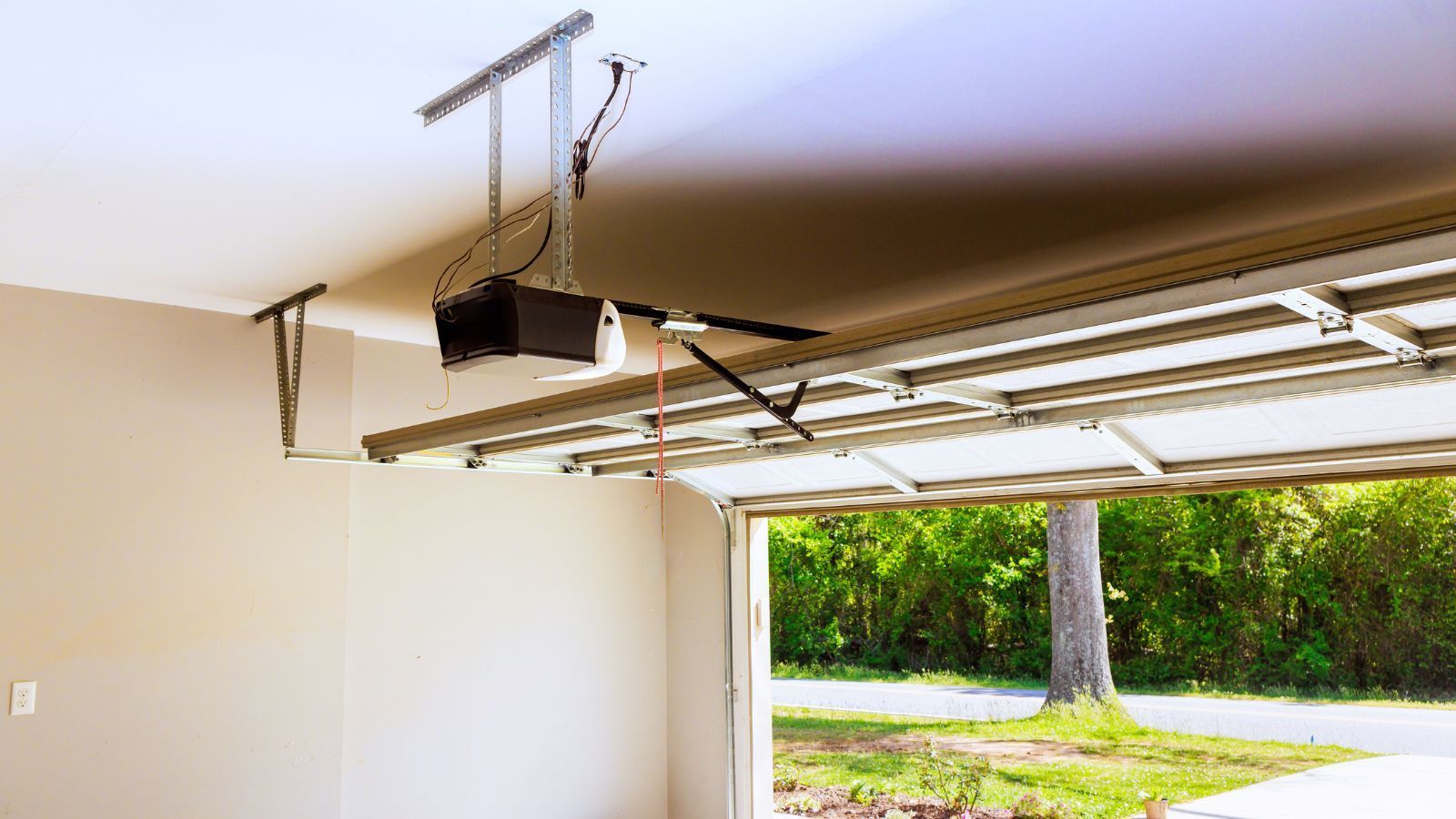 Open garage with raised door, ceiling-mounted garage door opener, and a driveway view outside