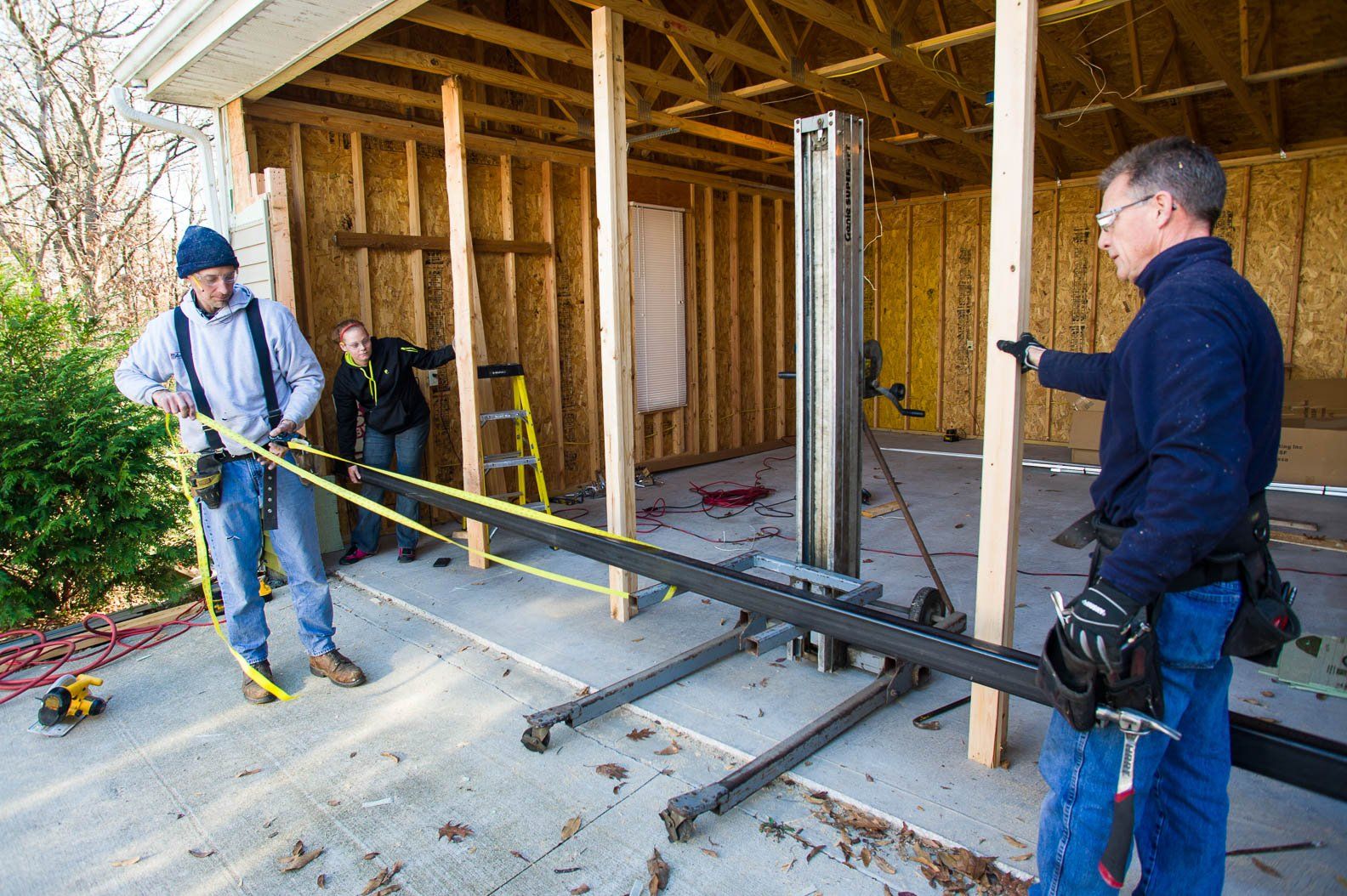 Workers measuring a house foundation inside a framed construction site with a tape measure and level