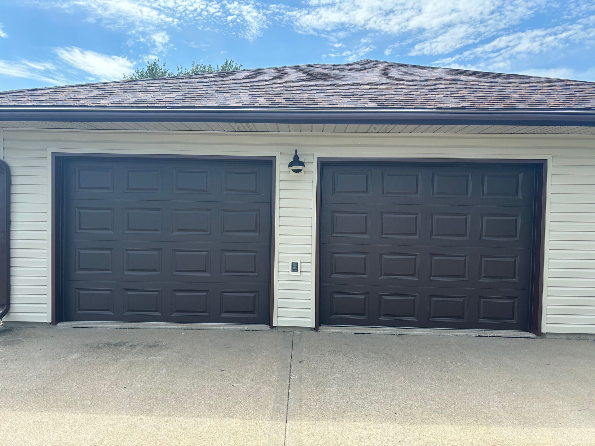 Two dark gray garage doors on a beige house exterior with a white trim and driveway in front