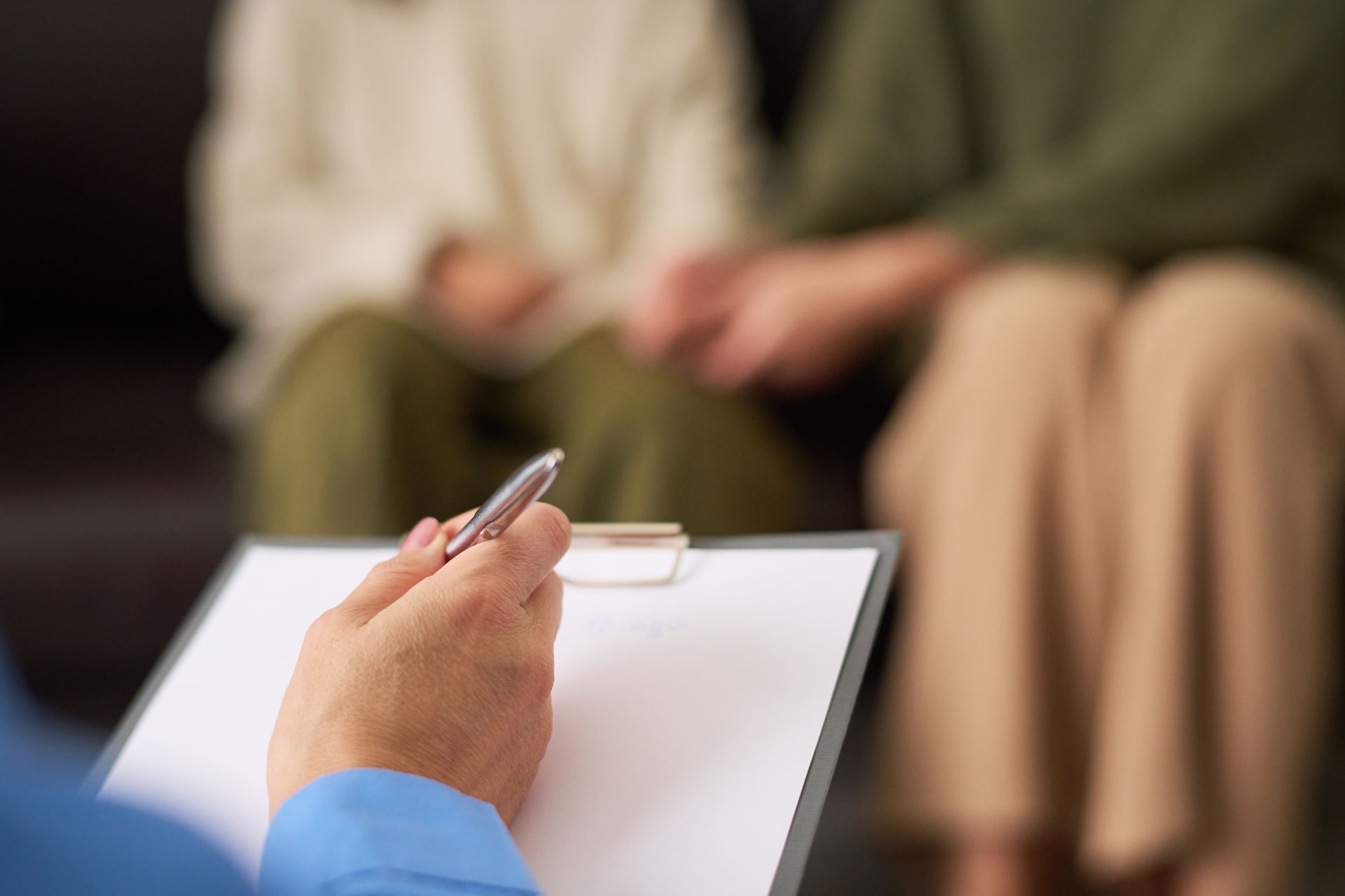 Couple holding hands during therapy session; therapist taking notes.