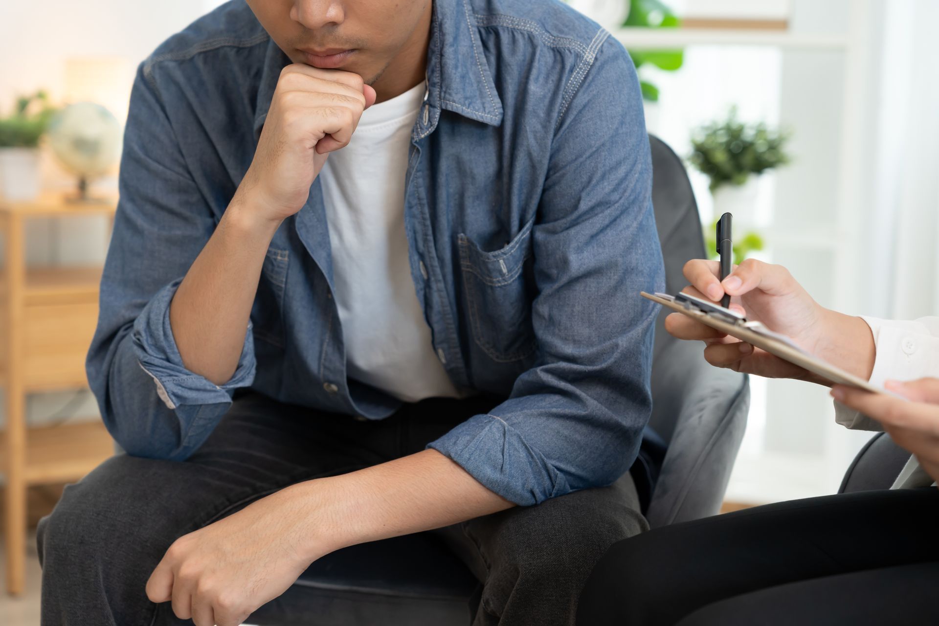 Man in therapy session; holding chin, listening to notes being taken.
